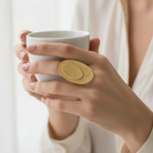 Hand holding a white mug with a gold ring on a blurred background