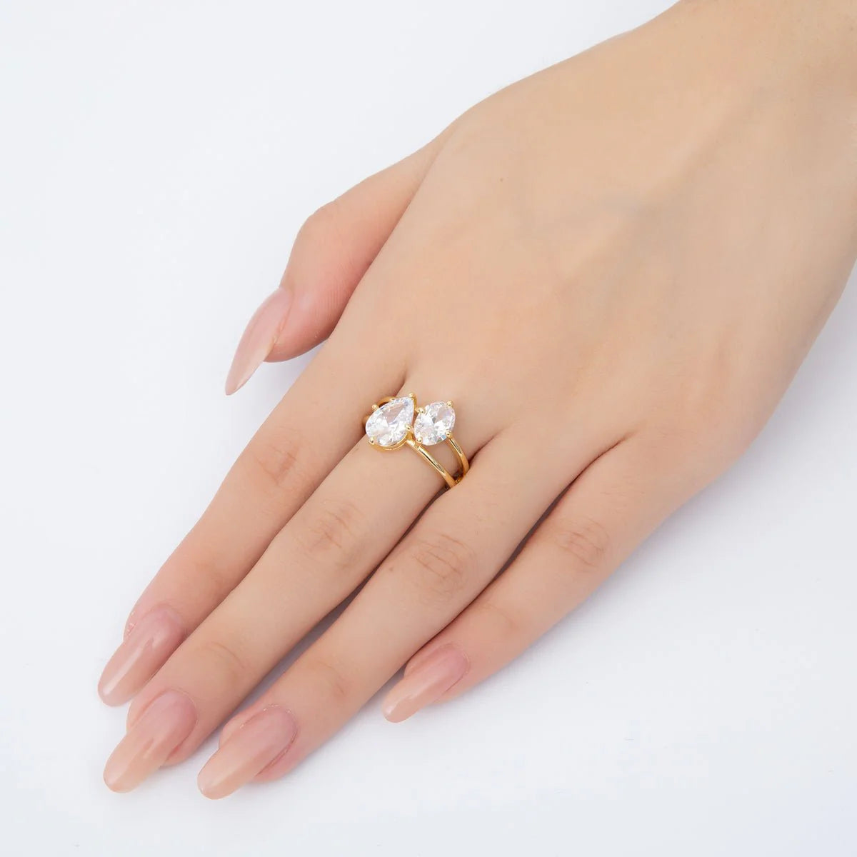 Gold ring with two clear stones on a hand against a white background