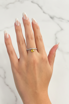 Hand wearing a ring with a yellow gemstone on a marble background