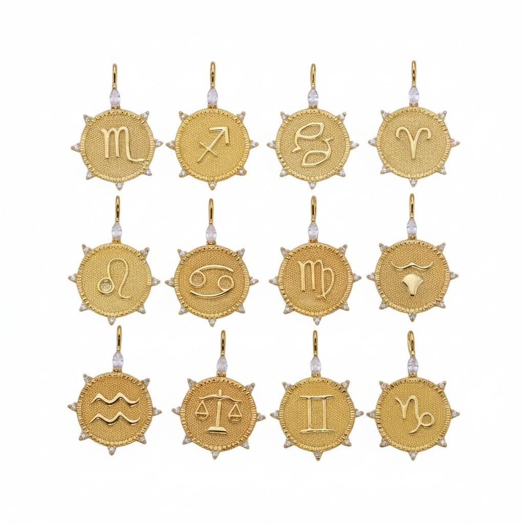 Twelve gold zodiac sign pendants arranged in a 3x4 grid on a light gray background. Each pendant is a round textured gold medallion with a different zodiac symbol, small clear crystal accents, and a top loop for hanging.