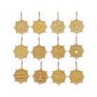 Twelve gold zodiac sign pendants arranged in a 3x4 grid on a light gray background. Each pendant is a round textured gold medallion with a different zodiac symbol, small clear crystal accents, and a top loop for hanging.