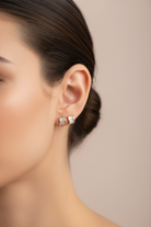 Close-up of a woman wearing diamond stud earrings against a neutral background