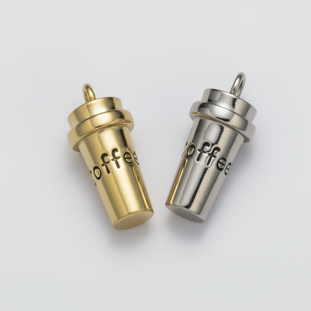 Two small coffee cup-shaped charms, one gold-toned and one silver-toned, both engraved with the word 'coffee' and shown on a plain light background.