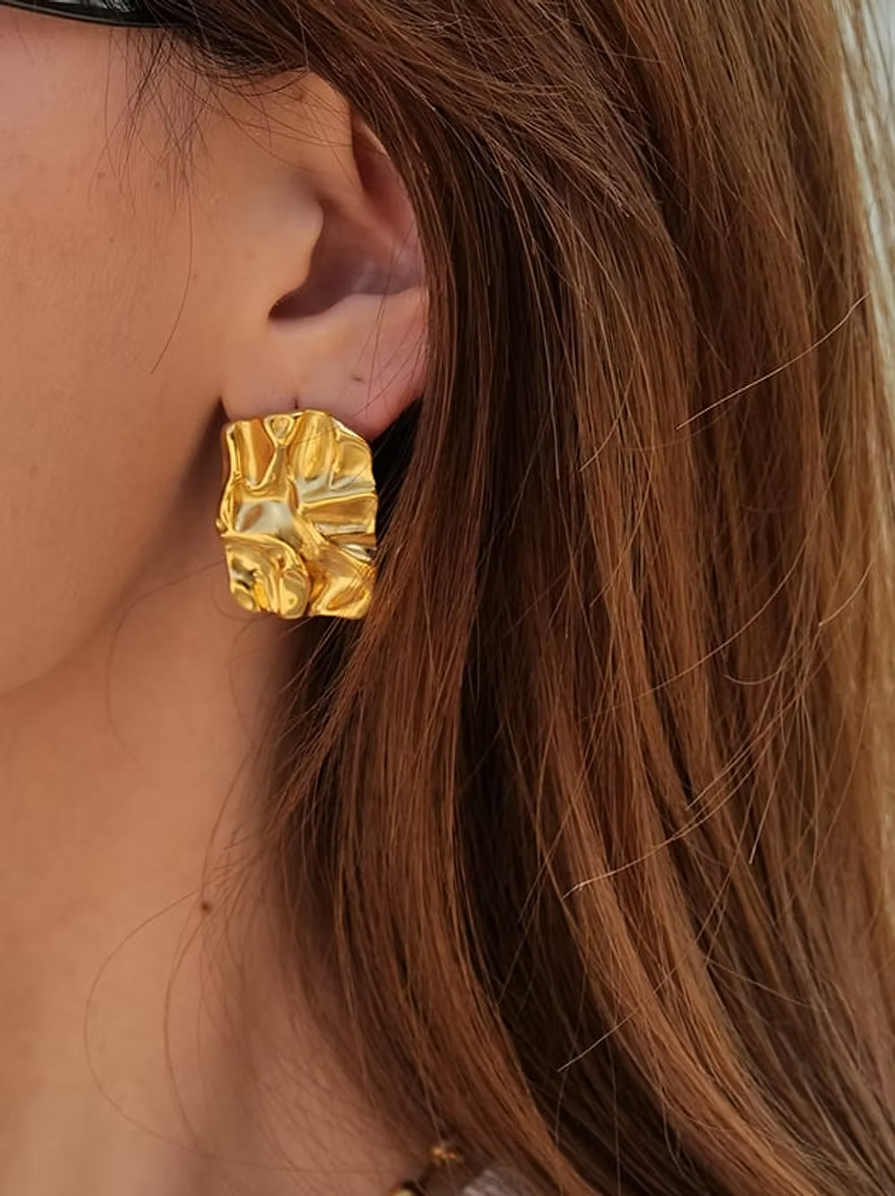 Close-up of a person wearing gold textured earrings with brown hair.