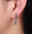 Silver hoop long stud earring worn on an ear with a blurred background