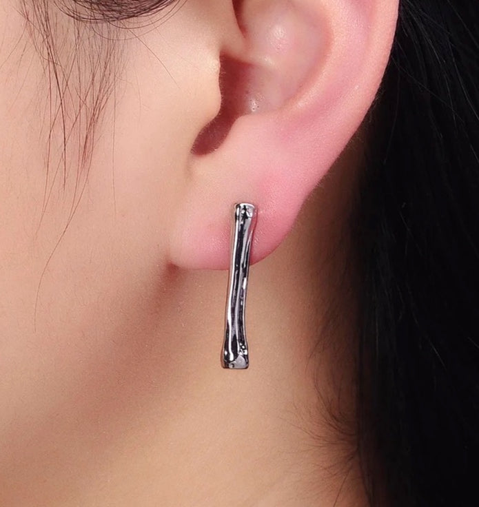 Silver hoop long stud earring worn on an ear with a blurred background