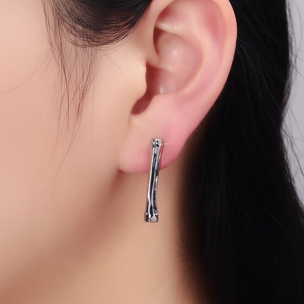 A close-up of a model's ear wearing a polished silver-toned curved hoop earring.