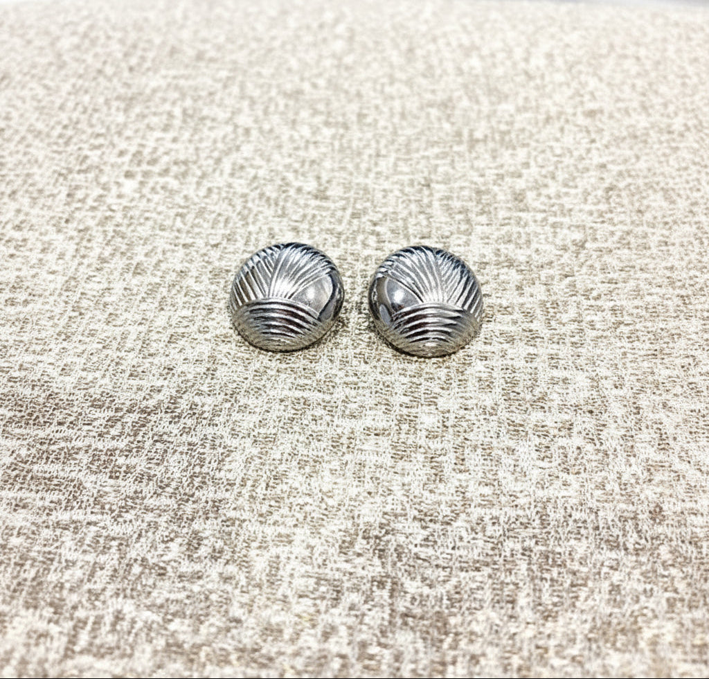 Pair of silver shell-shaped earrings on a textured beige surface