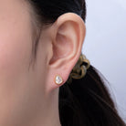 Close-up of an ear wearing a gold earring with a plain background