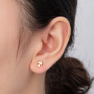 Gold earring worn on a person's ear with a neutral background