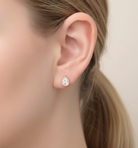 Close-up of an ear wearing a pear-shaped diamond earring on a neutral background