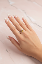 Hand wearing a ring with a yellow gemstone on a marble surface