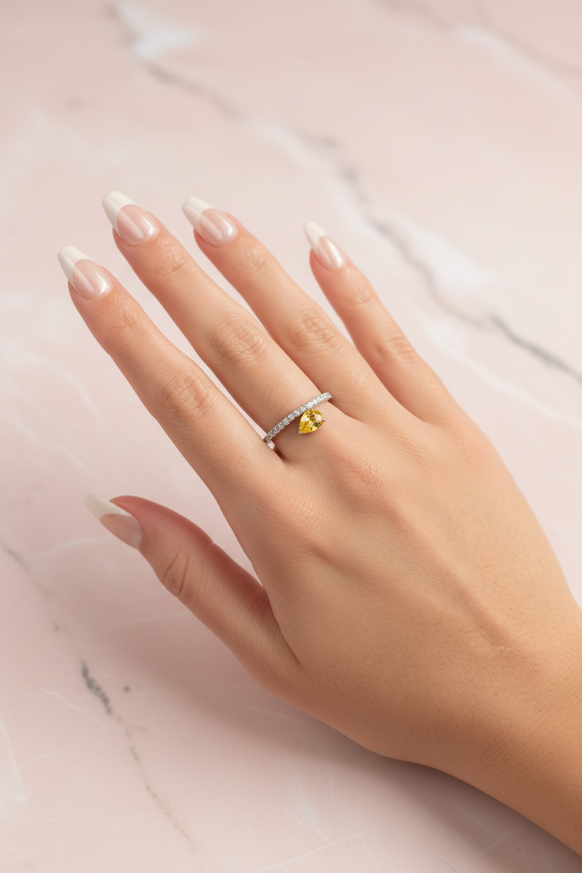 Hand wearing a ring with a yellow gemstone on a marble surface